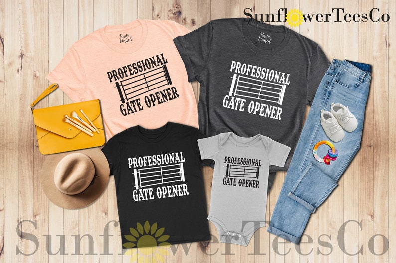 Op de afbeelding: Een set van vier t-shirts met een zwart-witte afbeelding van een poort met de tekst "Professional Gate Opener". De shirts zijn in verschillende kleuren, waaronder roze, grijs, zwart en lichtgrijs. De shirts zijn gerangschikt op een houten oppervlak met een spijkerbroek, een hoed en een handtas.