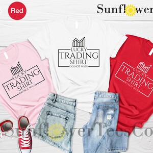 May include: Three t-shirts in pink, white, and red with a graphic design that says "Lucky Trading Shirt - Do Not Wash".