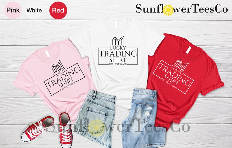 May include: Three t-shirts in pink, white, and red with a graphic design that says "Lucky Trading Shirt - Do Not Wash".