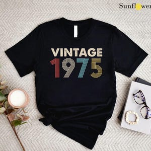 May include: Black t-shirt with the text "Vintage 1975" in rainbow colors. The numbers are in a retro font style.