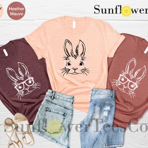 May include: Three t-shirts with a graphic of a bunny wearing glasses. The shirts are in heather maroon, peach, and mauve colors. The text "Sunflower TeesCo" is visible at the top of the image.