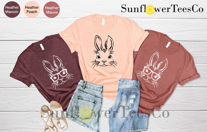 May include: Three t-shirts with a graphic of a bunny wearing glasses. The shirts are in heather maroon, peach, and mauve colors. The text "Sunflower TeesCo" is visible at the top of the image.