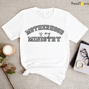 May include: White t-shirt with black text that reads "MOTHERHOOD is my MINISTRY" in a varsity-style font.