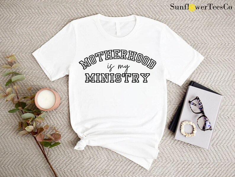 May include: White t-shirt with black text that reads "MOTHERHOOD is my MINISTRY" in a varsity-style font.