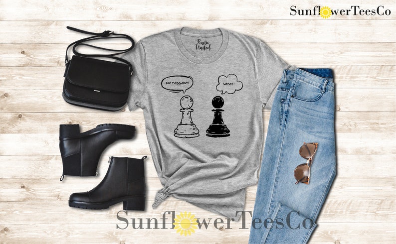 May include: A gray t-shirt with a graphic of two chess pieces. The white chess piece has a thought bubble above it that says "Say "Passant"!" and the black chess piece has a thought bubble above it that says "What?"
