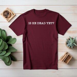 K&ouml;nnte beinhalten: Burgunderfarbenes T-Shirt mit wei&szlig;em Text, der "Is he dead yet?" lautet.