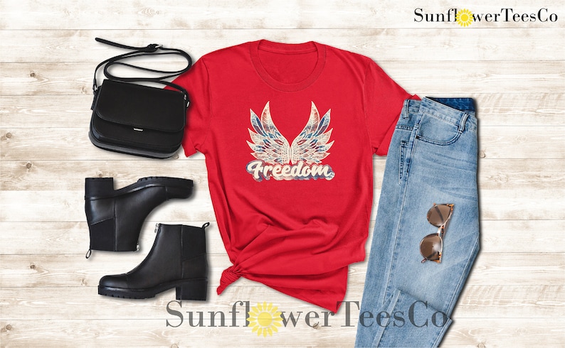 Puede incluir: Camiseta roja con un dise&ntilde;o de bandera estadounidense desgastado y la palabra "Freedom" en una fuente vintage.