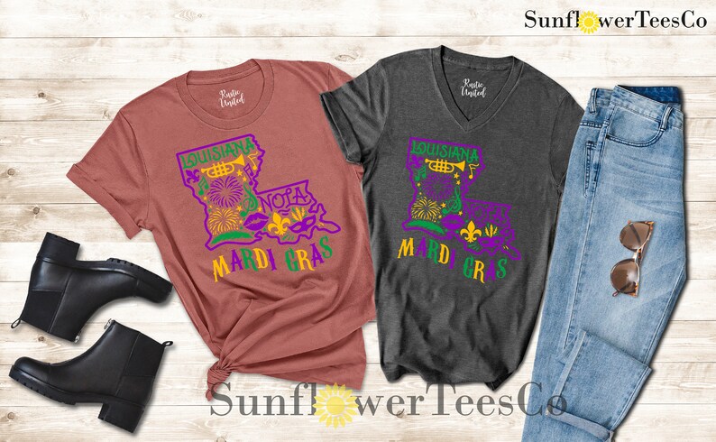 May include: Two t-shirts with a Mardi Gras theme. The left shirt is a rust color with a graphic of the state of Louisiana with the words "Louisiana", "NOLA", and "Mardi Gras". The right shirt is a dark gray with a similar graphic but with the words "Louisiana" and "Mardi Gras".