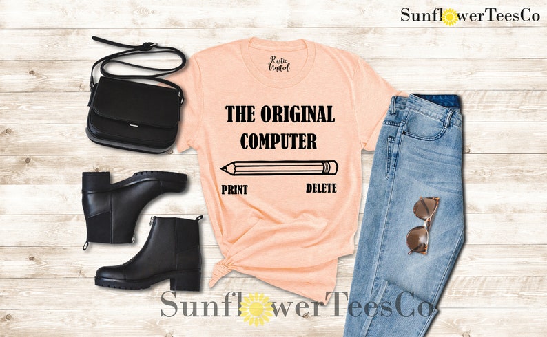 K&ouml;nnte beinhalten: Ein pfirsichfarbenes T-Shirt mit dem Text "THE ORIGINAL COMPUTER" und einem Bleistift mit den W&ouml;rtern "PRINT" und "DELETE" darunter. Das Shirt ist mit einer blauen Jeans, schwarzen Stiefeln und einer schwarzen Handtasche gestylt.