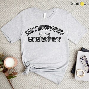 May include: Gray t-shirt with the text "MOTHERHOOD is my MINISTRY" in black lettering.