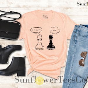 May include: A peach-colored t-shirt with a graphic of two chess pieces. The white chess piece has a thought bubble above it that says "En Passant!" and the black chess piece has a thought bubble above it that says "What?"