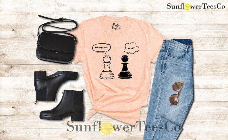 May include: A peach-colored t-shirt with a graphic of two chess pieces. The white chess piece has a thought bubble above it that says "En Passant!" and the black chess piece has a thought bubble above it that says "What?"