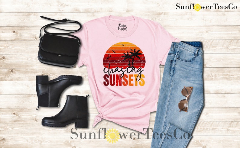 May include: Pink t-shirt with a retro sunset graphic and the text "chasing sunsets". The shirt is paired with blue jeans, black boots, and a black purse.