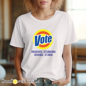 a woman wearing a vote t - shirt with the slogan, remove stubborn orange stains