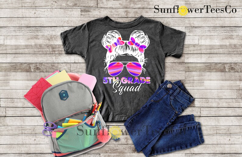 May include: A dark grey t-shirt with a white graphic of a girl with pigtails wearing sunglasses and the text "5th Grade Squad".