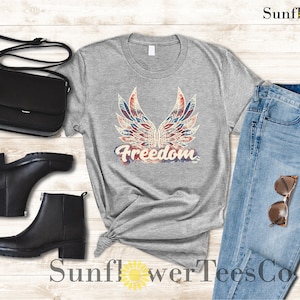 Puede incluir: Una camiseta gris con un gr&aacute;fico desgastado de alas rojas, blancas y azules con la palabra "Freedom" en una fuente de estilo acuarela descolorida.