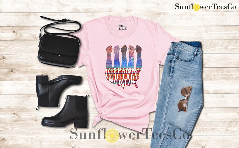May include: Pink t-shirt with a graphic of raised fists in front of a map of the United States. The graphic is colorful and includes the text "Hispanic Heritage Month".