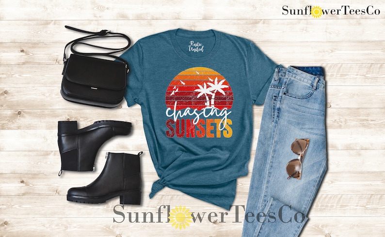 May include: A teal blue t-shirt with a vintage sunset graphic and the text "chasing sunsets". The shirt is paired with blue jeans, black ankle boots, and a black crossbody bag.