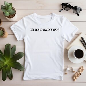 K&ouml;nnte beinhalten: Wei&szlig;es T-Shirt mit dem Aufdruck "IS HE DEAD YET?" in Schwarz auf der Vorderseite.