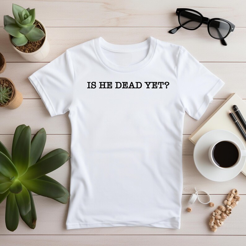 K&ouml;nnte beinhalten: Wei&szlig;es T-Shirt mit dem Aufdruck "IS HE DEAD YET?" in Schwarz auf der Vorderseite.