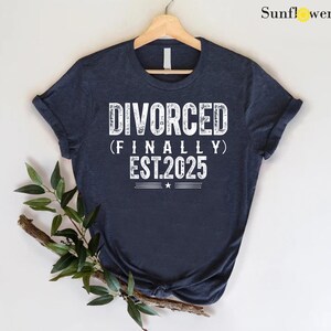 May include: A navy blue t-shirt with white text that reads "DIVORCED (FINALLY) EST.2025".