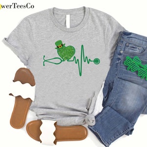 May include: A gray t-shirt with a green shamrock heart and a stethoscope, representing a heartbeat. The heart is wearing a green leprechaun hat.