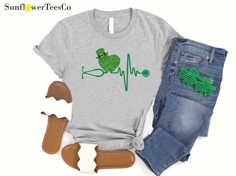 May include: A gray t-shirt with a green shamrock heart and a stethoscope, representing a heartbeat. The heart is wearing a green leprechaun hat.