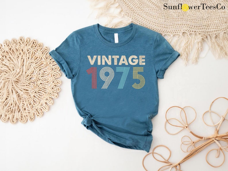 May include: A teal blue t-shirt with the text "Vintage 1975" in a retro font with colorful stripes.