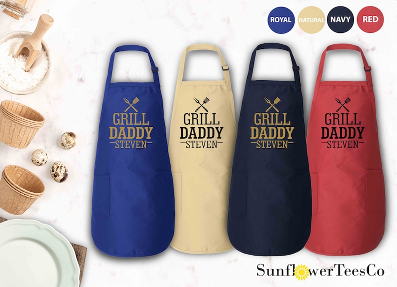 May include: Four aprons in different colors: royal blue, natural beige, navy blue, and red. Each apron has a pocket and the text "Grill Daddy -Steven-  " with crossed grilling utensils.