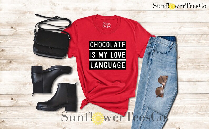 May include: A red t-shirt with the text "CHOCOLATE IS MY LOVE LANGUAGE" in a black and white rectangular design. The image also includes black ankle boots, a black purse, light blue jeans, and sunglasses.