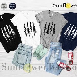 Op de afbeelding: Vier V-hals T-shirts met een afbeelding van een rij van vijf dennenbomen. De shirts zijn in zwart, wit, grijs melange en marineblauw. De tekst "SunflowerTeesCo" staat bovenaan de afbeelding.