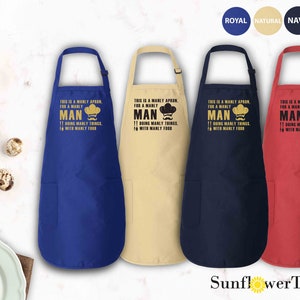 May include: Four kitchen aprons in different colors: royal blue, natural beige, navy blue, and red. Each apron has a pocket and a printed design that says "This is a manly apron for a manly man doing manly things with manly food".