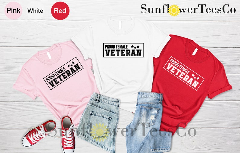 May include: Three t-shirts in pink, white, and red with the text "PROUD FEMALE*** VETERAN" printed on each. The shirts are laid out on a wooden surface with denim shorts.