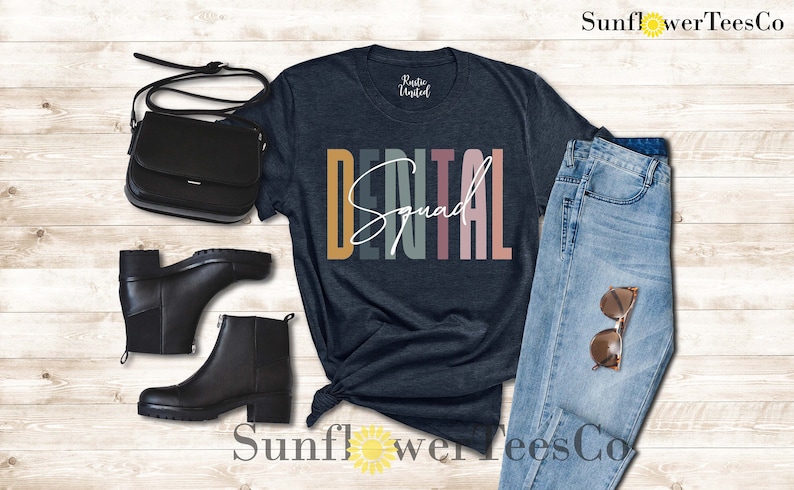 May include: A dark blue t-shirt with the text "DENTAL Squad" in colorful stripes. The shirt is styled with black boots, a black purse, and blue jeans.
