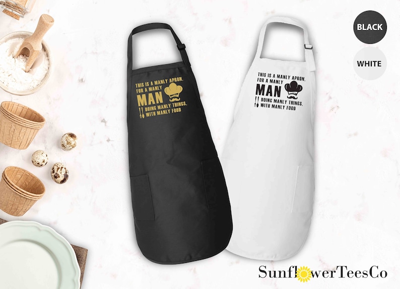 May include: Two black and white aprons with a pocket. The aprons have a gold graphic with the text "This is a manly apron for a manly man doing manly things with manly food".