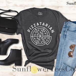 May include: A dark gray t-shirt with the text "Pizzatarian" in white lettering. The text is above a graphic of a pizza slice with white outlines.