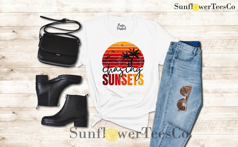 May include: White t-shirt with a retro sunset graphic and the text "chasing sunsets". The shirt is paired with blue jeans, a black crossbody bag, and black ankle boots.