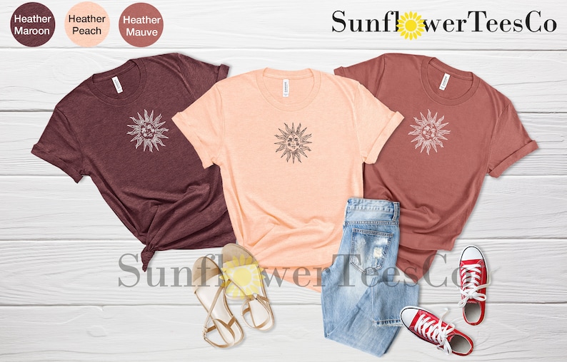 May include: Three t-shirts with a sun graphic design in maroon, peach, and rust colors. The shirts are laid out on a wooden surface with a pair of sandals and jeans. The text "Sunflower TeesCo" is visible at the top of the image.