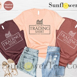 May include: Three t-shirts in different colors, maroon, peach, and rust, with a white graphic that says "Lucky Trading Shirt - Do Not Wash".