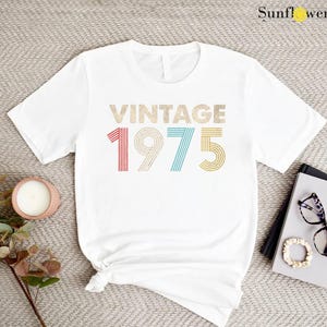 May include: White t-shirt with the text "Vintage 1975" in rainbow colors. The numbers are in a retro font style.