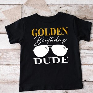 a black shirt with a gold birthday dude on it
