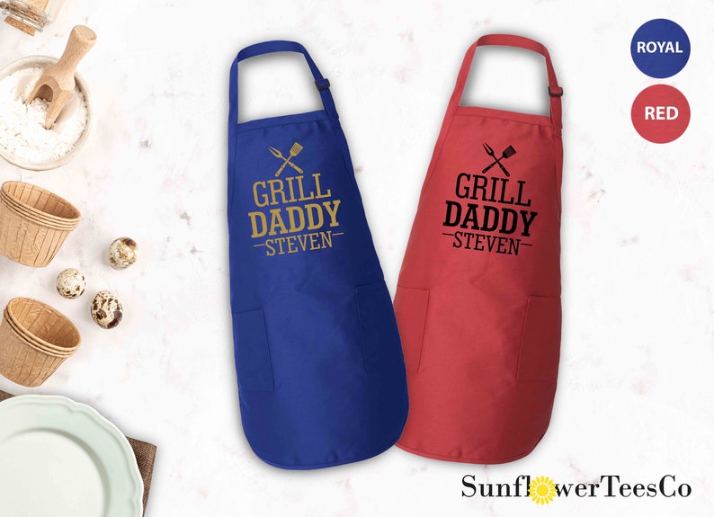 May include: Two aprons with adjustable neck straps and a large pocket. The aprons are blue and red. The text on the aprons reads "Grill Daddy - Steven".
