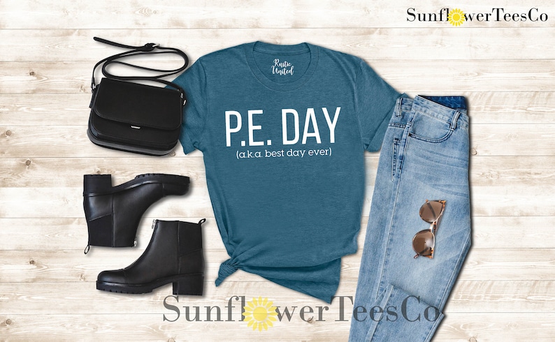 Op de afbeelding: Een tealblauw t-shirt met witte tekst die "P.E. DAY (a.k.a best day ever)" luidt. Het shirt is gestyled met een blauwe jeans, zwarte laarzen en een zwarte handtas.