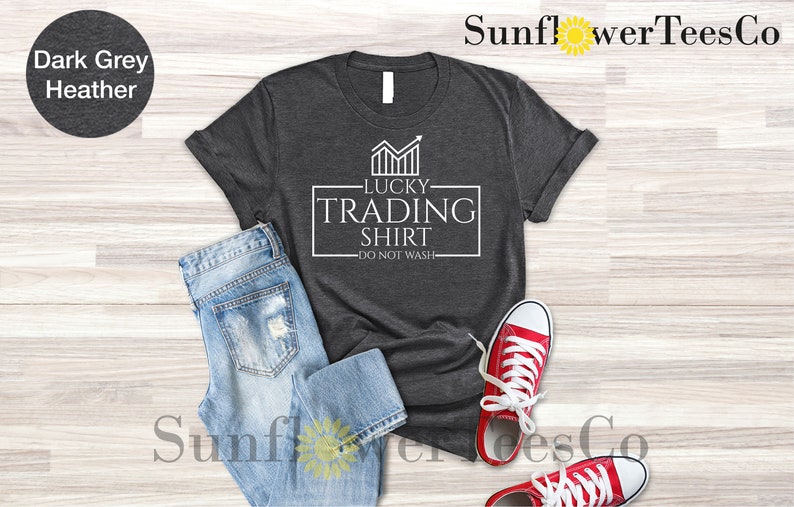 May include: A dark heather grey t-shirt with a white graphic that says "Lucky Trading Shirt - Do Not Wash". The graphic features a stylized chart with an upward arrow.