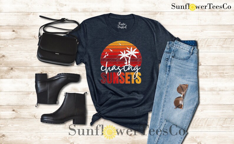 May include: A navy blue t-shirt with a vintage sunset graphic and the text "chasing sunsets". The graphic features palm trees and birds flying over a red, orange, and yellow sunset.