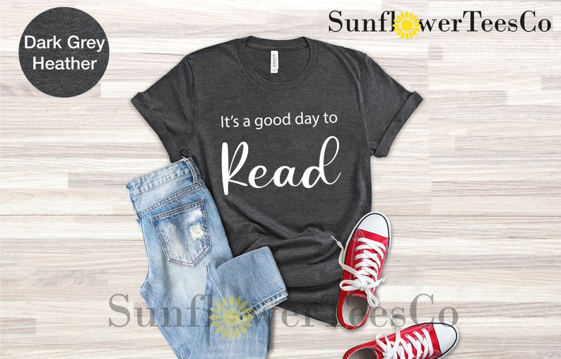 Op de afbeelding: Donkergrijs gem&ecirc;leerd T-shirt met de witte tekst "It's a good day to Read". Het shirt wordt gecombineerd met lichtblauwe jeans en rode sneakers met witte veters en zolen. Het shirt is van SunflowerTeesCo.