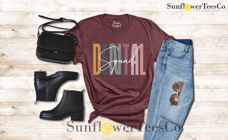 May include: A maroon t-shirt with the text "DENTAL Squad" in colorful letters. The shirt is styled with a pair of black boots, a black purse, and blue jeans.