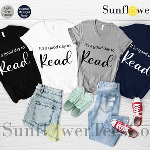 Op de afbeelding: Vier V-hals T-shirts in zwart, wit, lichtgrijs heather en marineblauw, elk met de tekst "It's a good day to Read" in witte letters. De shirts worden getoond met denim shorts, jeans en sneakers.