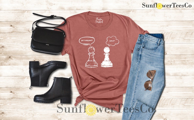 May include: A maroon t-shirt with a white graphic of two chess pieces. The white piece is thinking "Wait!" and the black piece is thinking "En Passant!"