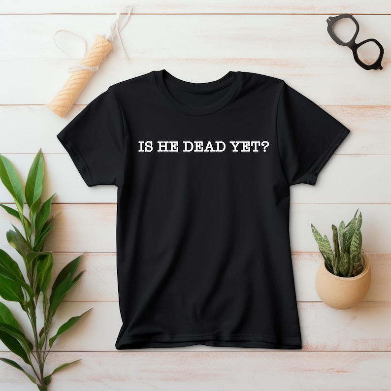 K&ouml;nnte beinhalten: Schwarzes T-Shirt mit wei&szlig;em Text, der "IS HE DEAD YET?" lautet.